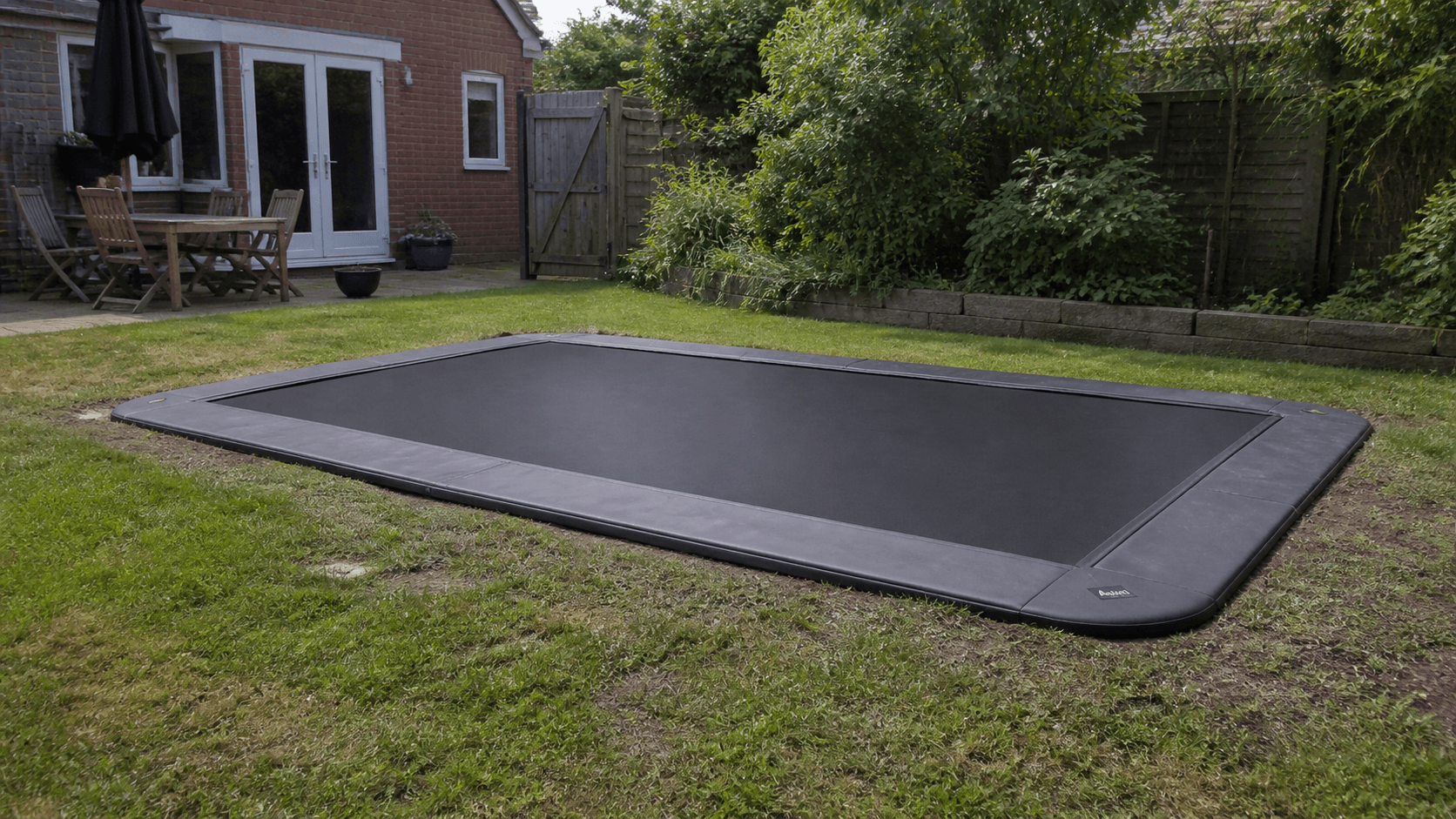A rectangular in-ground trampoline installed flush with a backyard lawn.