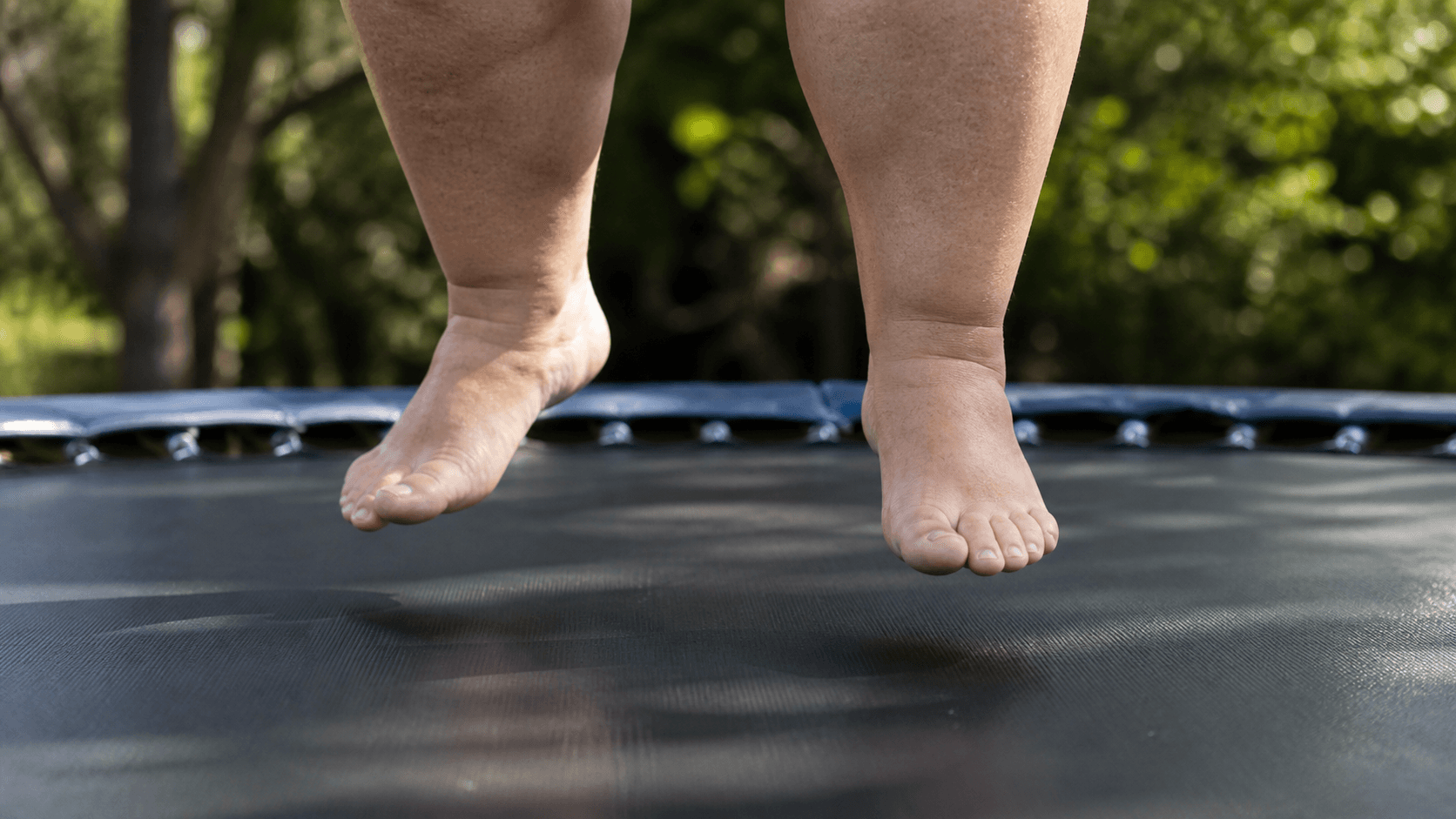 Close-up of an adult bouncing on a trampoline mat outdoors.
