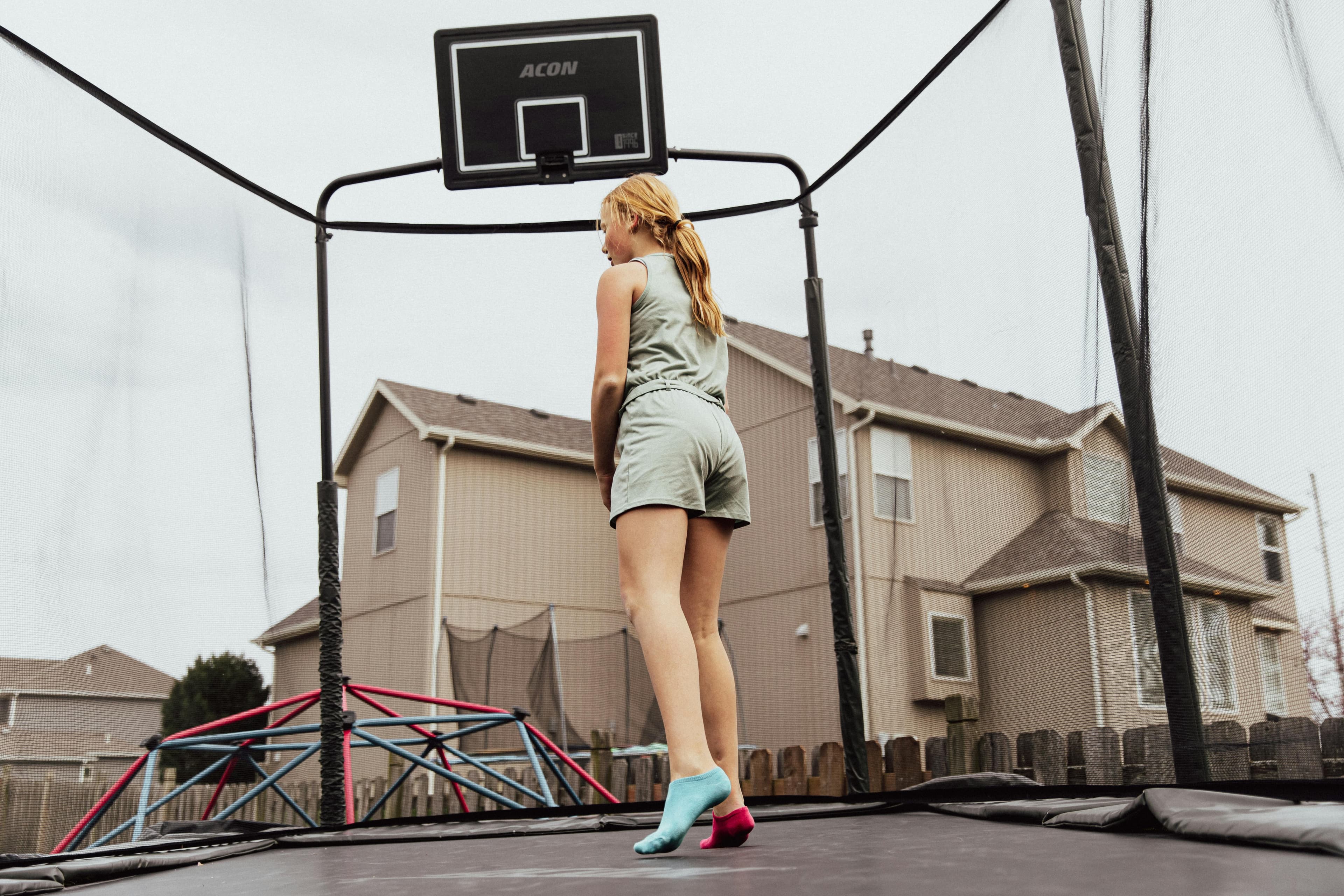A teenage girl bouncing on an outdoor backyard trampoline.
