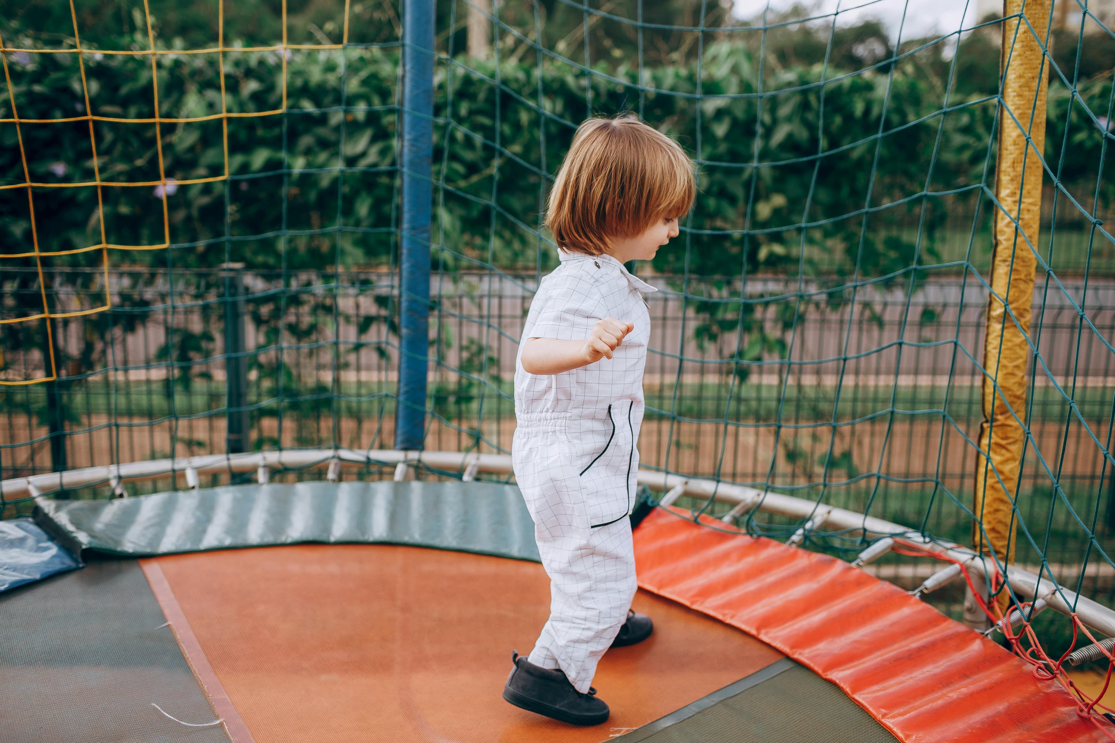 A toddler standing inside a small enclosed outdoor trampoline.